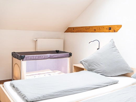 Reisebett für Babys neben einem gemachten Bett mit hellgrauer Bettwäsche im Schlafzimmer