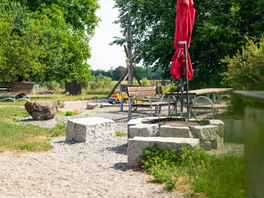 Grillplatz mit Granitblöcken und Sitzgelegenheiten im Grünen, im Hintergrund ein roter Sonnenschirm