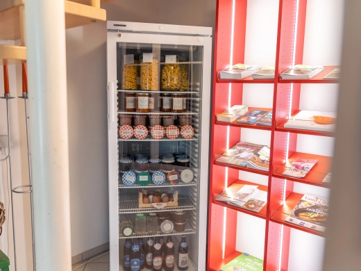 Hofladen mit Kühlschrank voller Gläser und Flaschen, daneben rote Regale mit Flyer