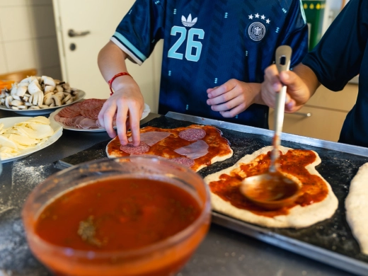 Pizzateig auf dem Backblech wird mit Tomatensauce bestrichen, daneben eine Schüssel Sauce