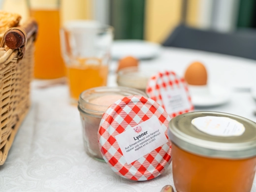Gedeckter Frühstückstisch mit Marmeladengläsern mit rot-weißen Deckeln, Orangensaft und Frühstücksei