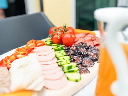 Frühstücksplatte mit Wurst, Käse, Gurken und Tomaten, im Hintergrund Orangensaft