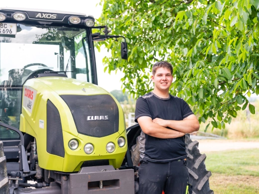 Constantin Häckler steht mit verschränkten Armen vor einem gelbgrünen Traktor unter einem Baum