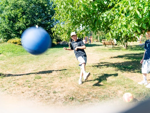 Junge mit heller Mütze kickt auf der Wiese einen Fußball, im Vordergrund ein unscharfer blauer Ball