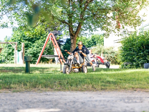 Kinder fahren auf Kettcars über das Gelände, im Hintergrund Bäume und Spielgeräte
