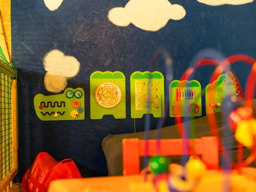 Kleinkindbereich der Spielscheune mit bunten Wandspielen vor blauer Wand mit Wolken