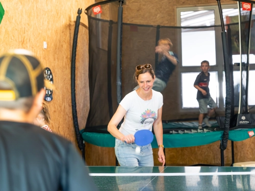 Frau spielt in der Spielscheune Tischtennis, im Hintergrund ein Trampolin mit Netz