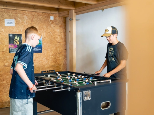 Zwei Jugendliche spielen in der Spielscheune am Kicker, im Hintergrund eine Holzwand