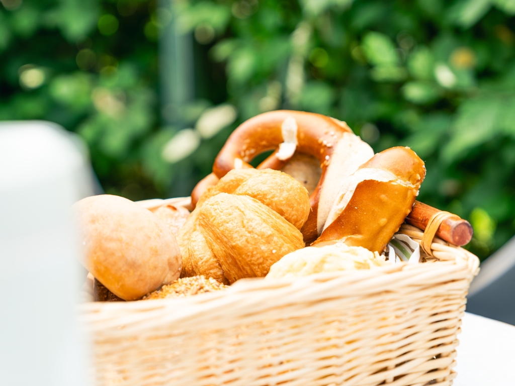Brötchenkorb mit frischen Brötchen und Brezeln auf dem Frühstückstisch im Freien