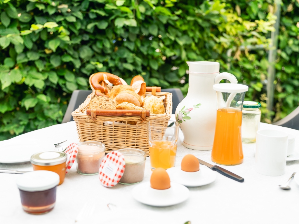 Gedeckter Frühstückstisch im Grünen mit Brötchenkorb, Orangensaft, Marmelade und Eiern