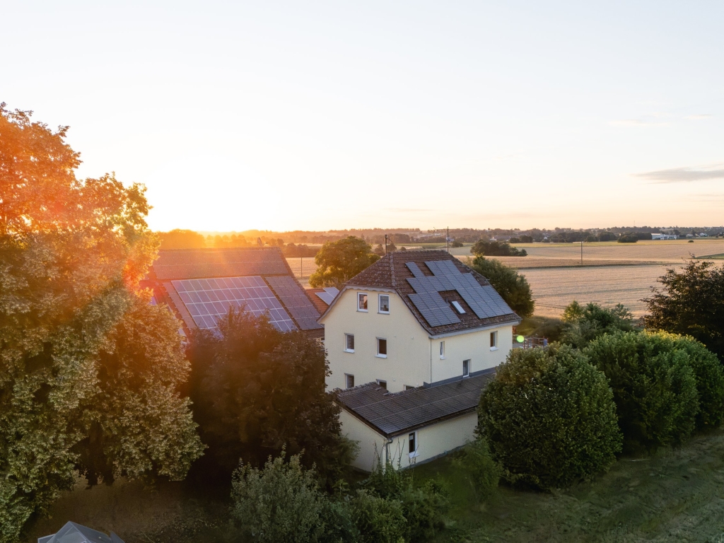 Ferienhof Häckler bei Sonnenaufgang aus der Luft, davor Bäume im Morgenlicht, dahinter Felder