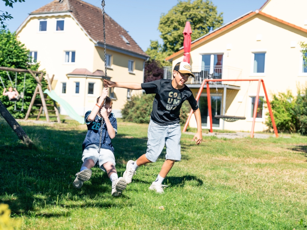 Kinder auf der Seilbahn vor den Gebäuden des Ferienhofs, im Hintergrund Spielgeräte