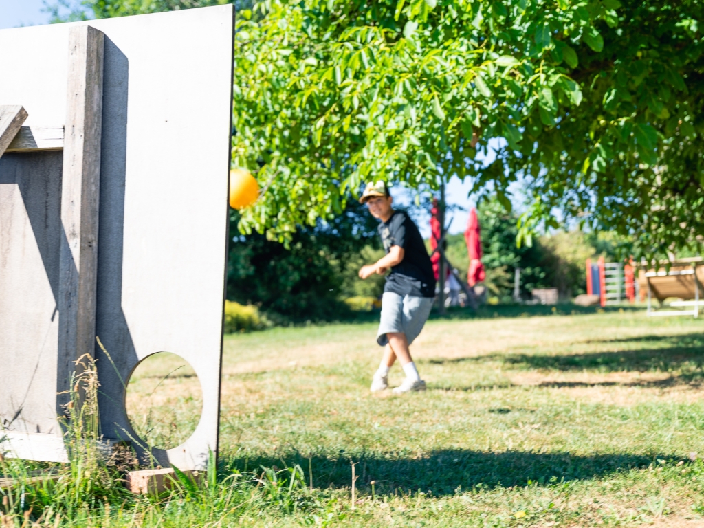 Kind spielt Fußball auf Wiese, im Vordergrund eine Zielscheibe, im Hintergrund Spielgeräte