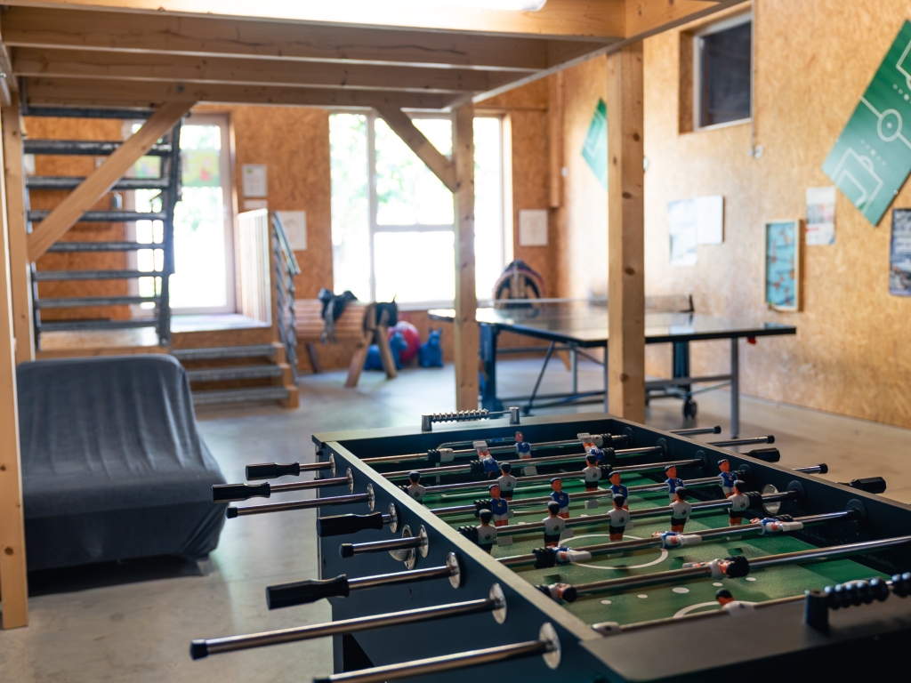Beheizte Spielscheune mit Kicker im Vordergrund, dahinter Holztreppe und Tischtennisplatte