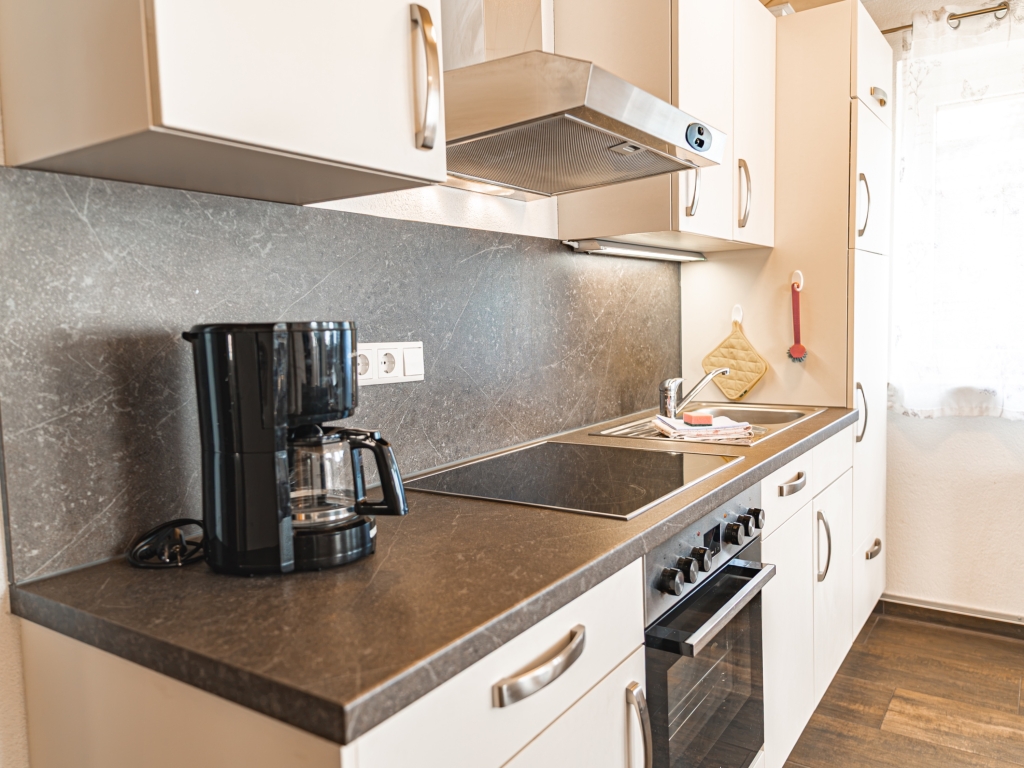 Ferienwohnung 10: Küchenzeile mit Herd, Backofen, Dunstabzug, Kaffeemaschine und dunklem Spritzschutz