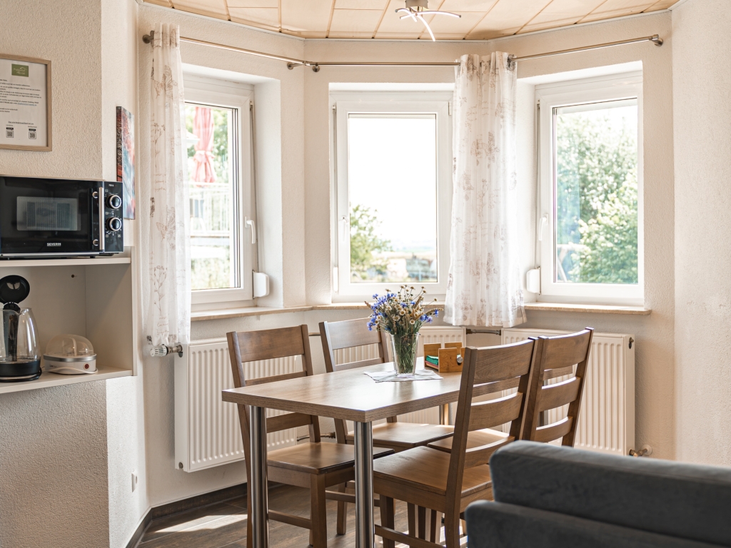 Ferienwohnung 10: Esstisch mit Stühlen am Erkerfenster, Blumenstrauß auf dem Tisch, links die Küchenzeile