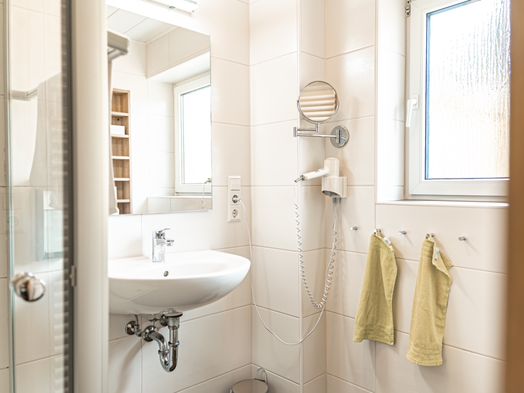 Ferienwohnung 10: Helles Badezimmer mit Waschbecken, Spiegel, Fenster und gelben Handtüchern an der Wand
