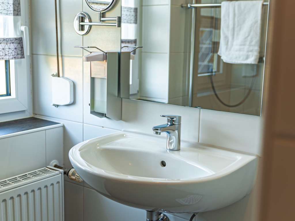 Ferienwohnung 11: Badezimmer mit Waschbecken, Spiegel mit Leuchte, Heizkörper und Handtuch an der Wand