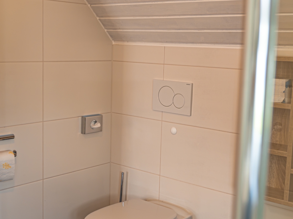 Ferienwohnung 11: WC-Raum mit Wand-WC, Spülkasten-Platte, hellen Fliesen und Dachschräge