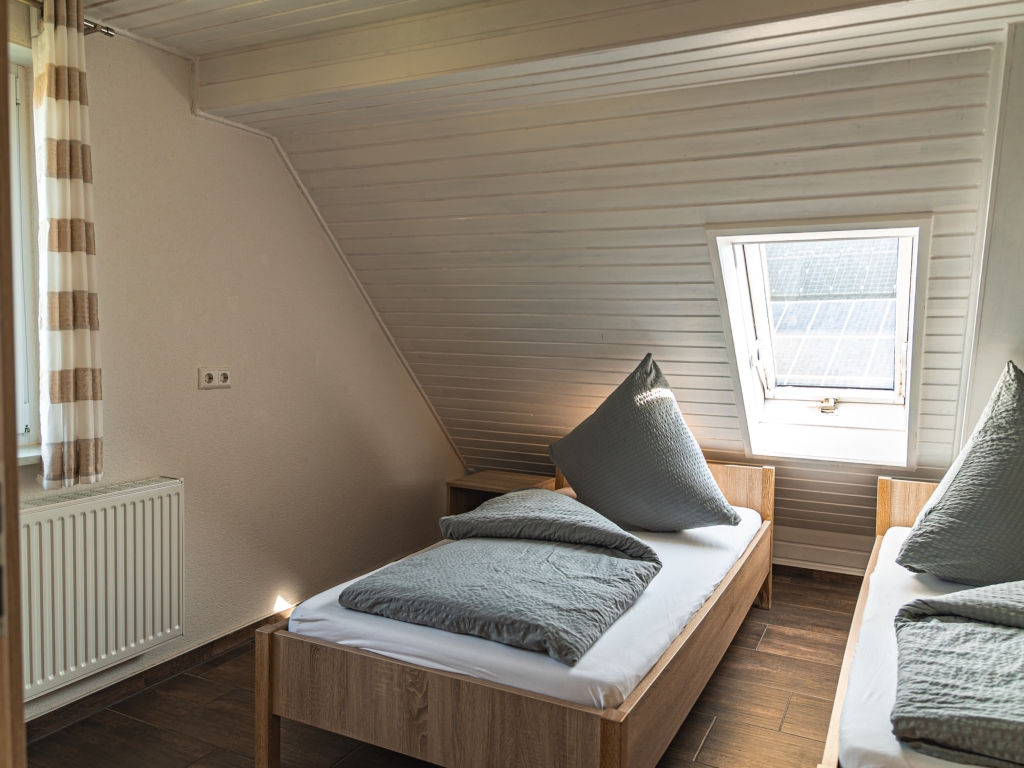 Ferienwohnung 11: Dachzimmer mit zwei Einzelbetten, Dachschräge mit Fenster und gestreiftem Vorhang