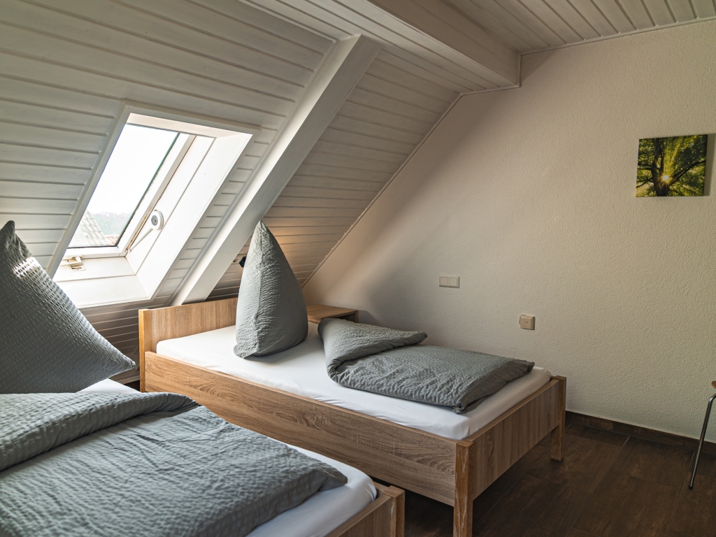 Ferienwohnung 11: Dachzimmer mit zwei Betten, grauer Bettwäsche und Dachfenster, Bild an der Wand