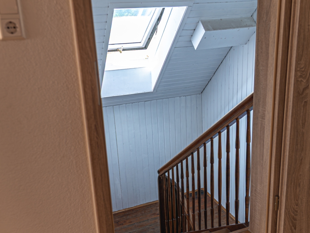 Ferienwohnung 11: Treppenabgang mit Holzgeländer, Holzverkleidung und Dachfenster im Treppenhaus