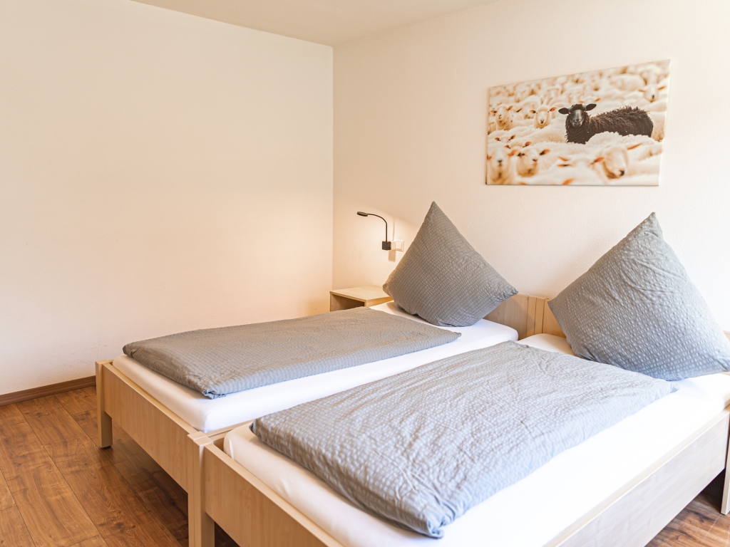 Ferienwohnung 1: Schlafzimmer mit zwei Betten, Leselampe und Schafbild an der Wand