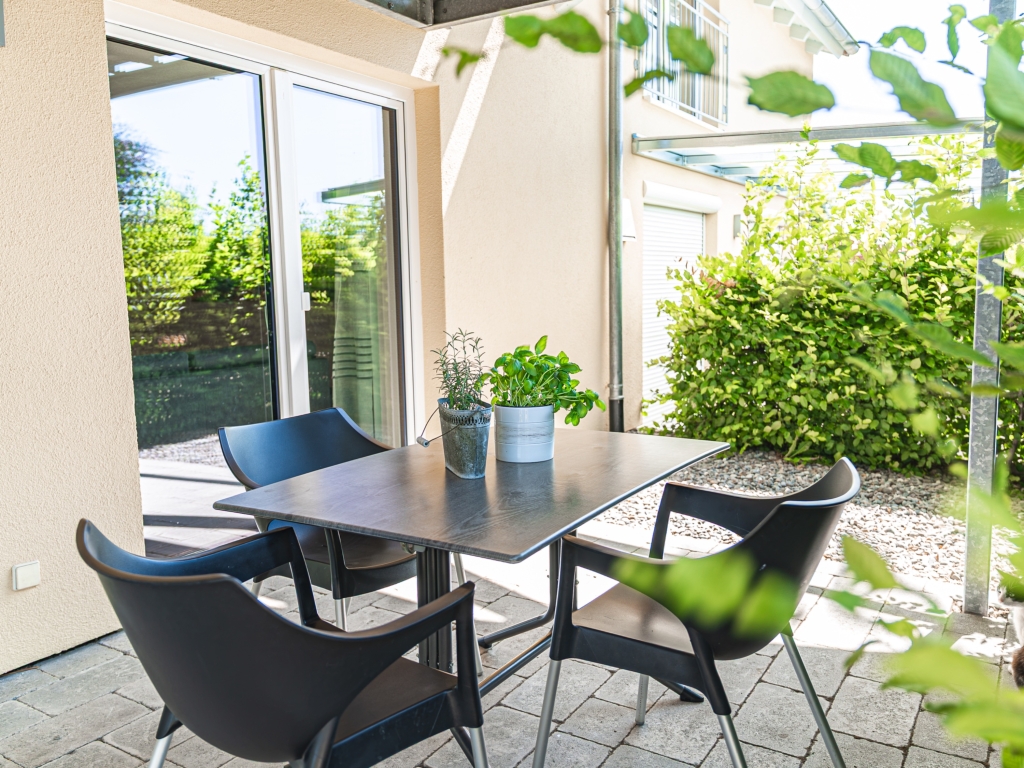 Ferienwohnung 1: Sitzplatz auf der Terrasse mit Tisch, Stühlen und Kräutertöpfen vor einer Hecke
