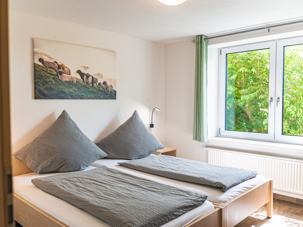Ferienwohnung 2: Schlafzimmer mit zwei Betten in grauer Bettwäsche, Wandbild und Fenster mit grünem Vorhang