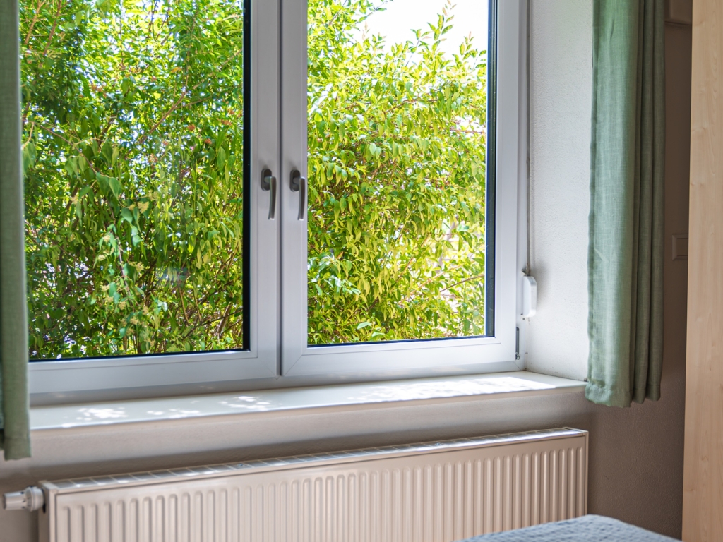 Ferienwohnung 2: Schlafzimmerfenster mit Blick ins Grüne, darunter Heizkörper und Bettkante