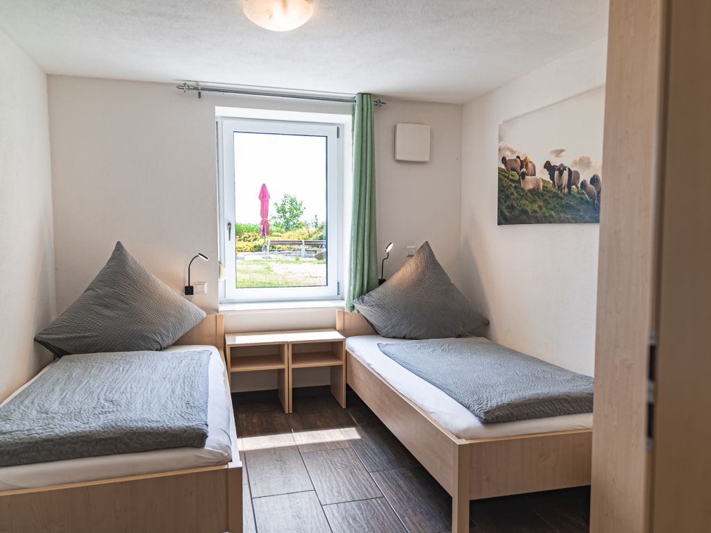 Ferienwohnung 2: Schlafzimmer mit zwei Einzelbetten, Nachttisch und Fenster mit grünem Vorhang