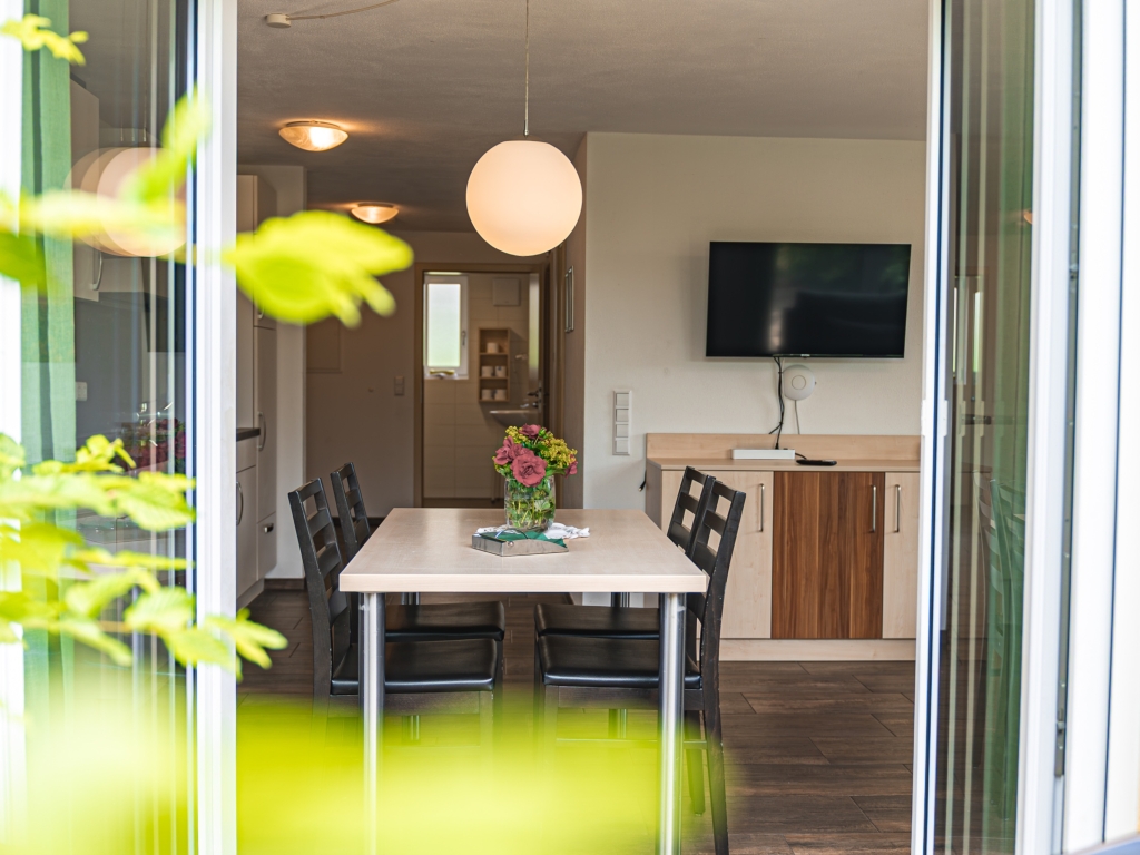 Ferienwohnung 2: Blick von der Terrasse in den Essbereich mit Esstisch, Blumenstrauß und Fernseher