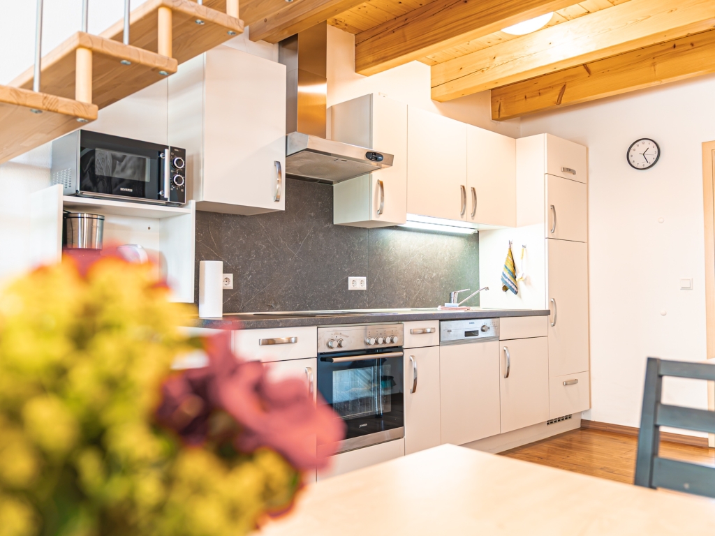 Ferienwohnung 3: Küchenzeile mit Backofen, Kochfeld, Dunstabzugshaube und Mikrowelle unter der Holzbalkendecke