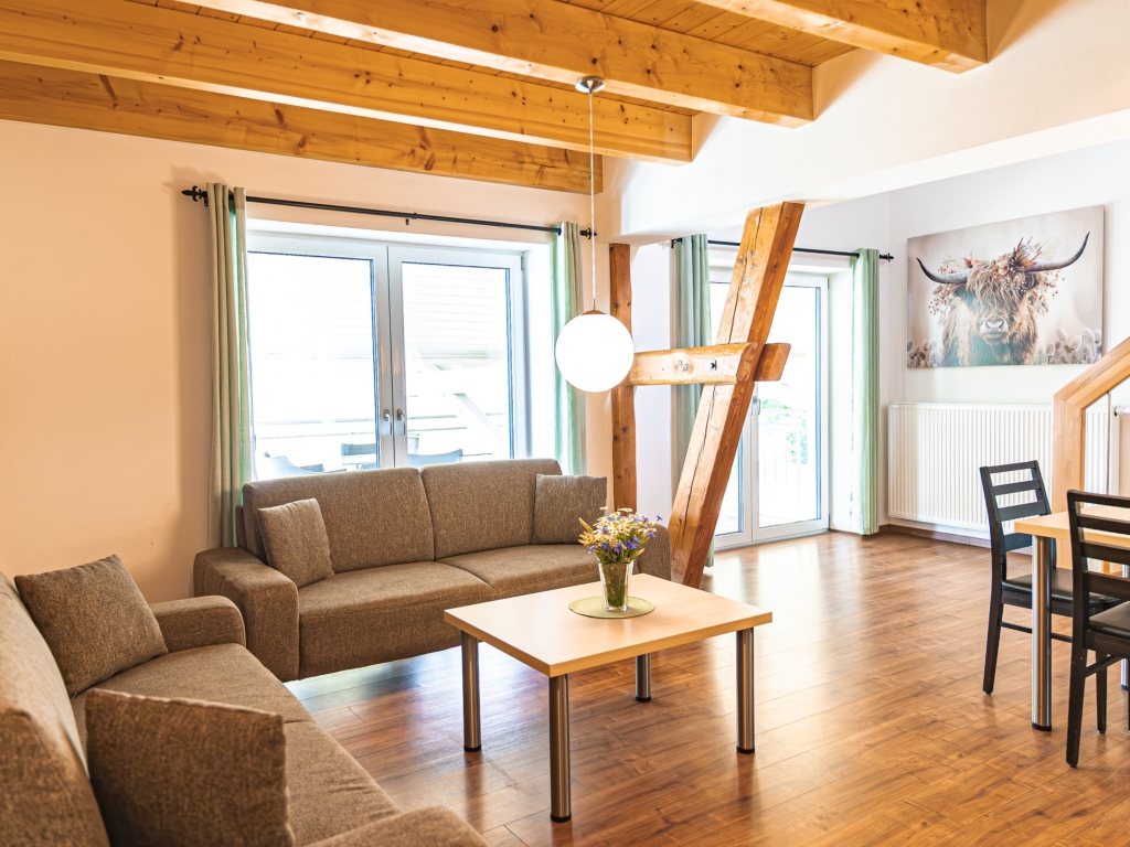 Ferienwohnung 3: Wohnbereich mit Sofa, Couchtisch und Rindbild an der Wand, daneben Holztreppe