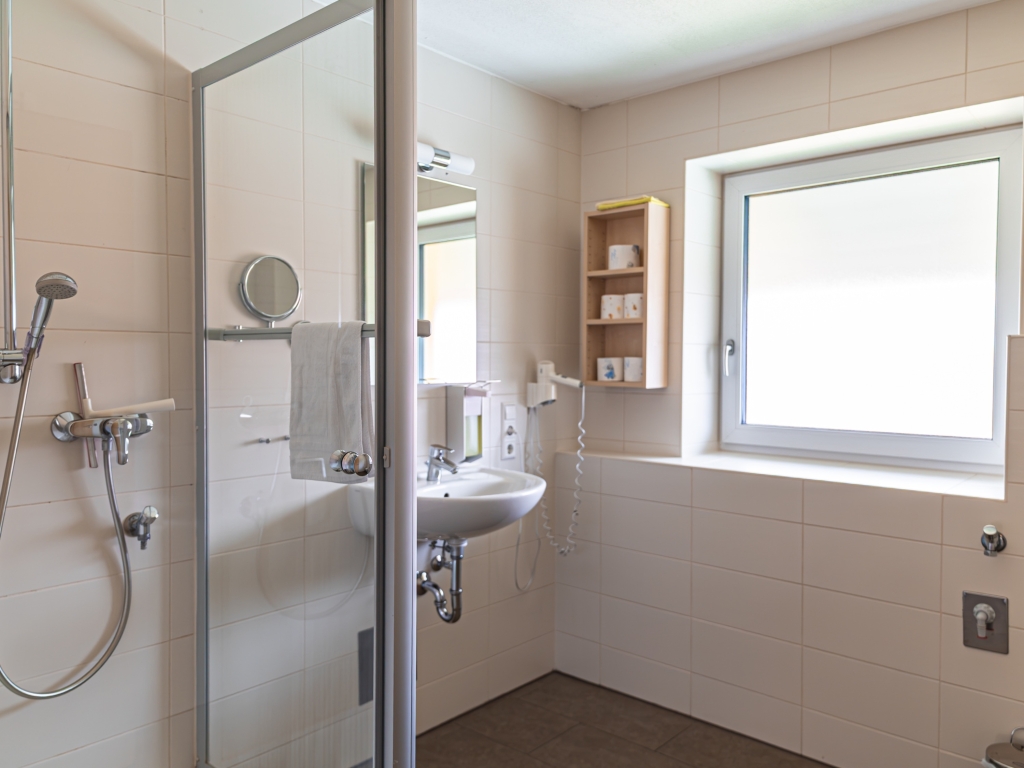 Ferienwohnung 3: Badezimmer mit Duschkabine, Waschbecken, Wandregal und Fenster