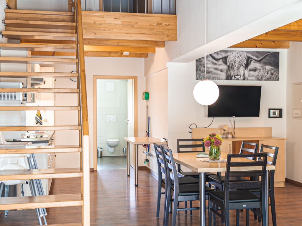 Ferienwohnung 3: Wohn-Essbereich mit Esstisch, Fernseher und offener Galerie mit Holztreppe darüber