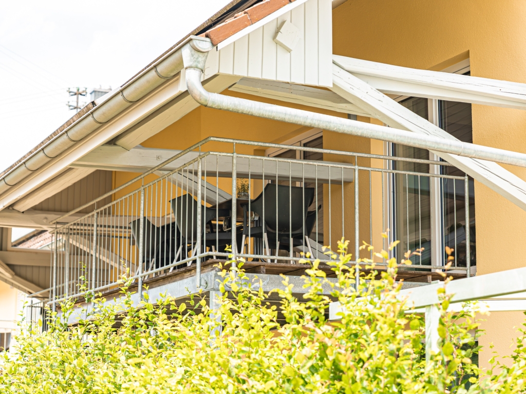 Ferienwohnung 3: Balkon mit Geländer an der Hausfassade, davor grüne Büsche