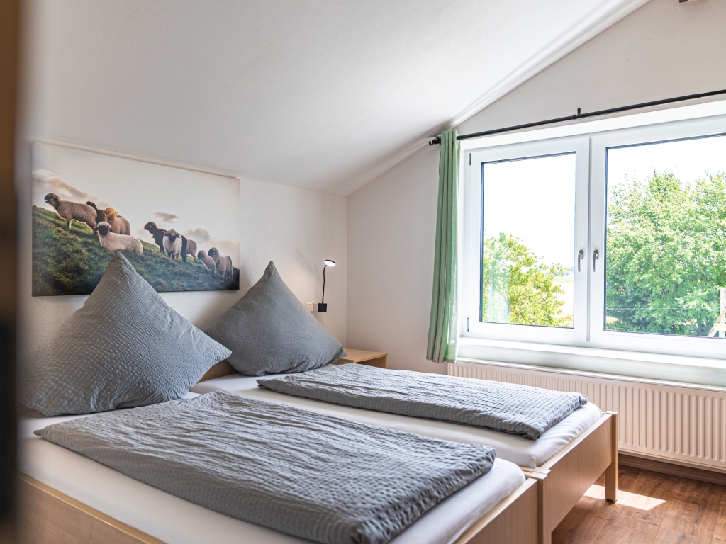 Ferienwohnung 4: Schlafzimmer unter der Dachschräge mit Betten in grauer Bettwäsche und Fenster mit grünem Vorhang