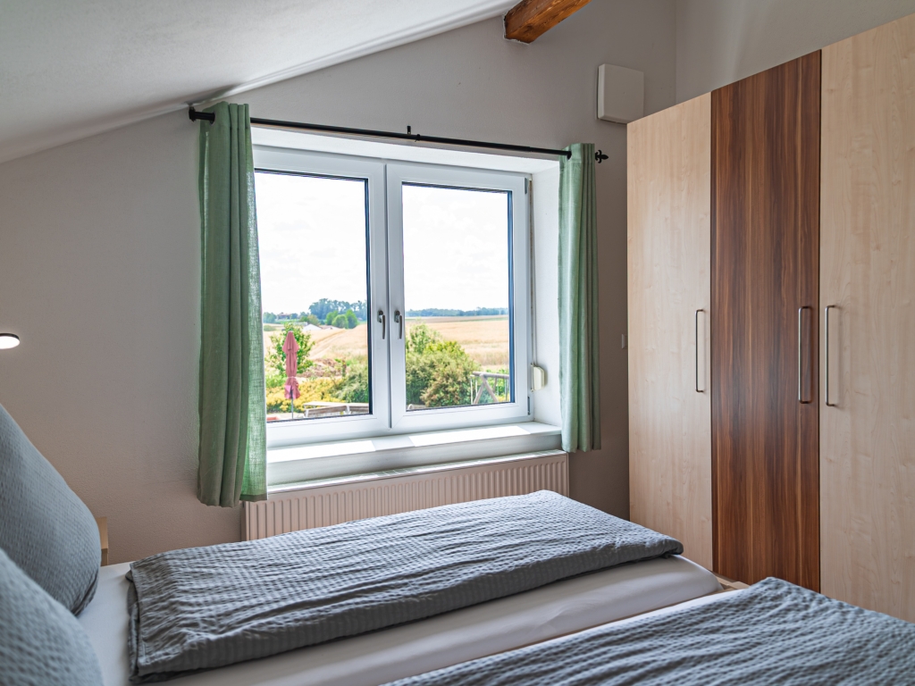 Ferienwohnung 4: Schlafzimmer mit Bett, Kleiderschrank und Fenster mit Blick über Felder