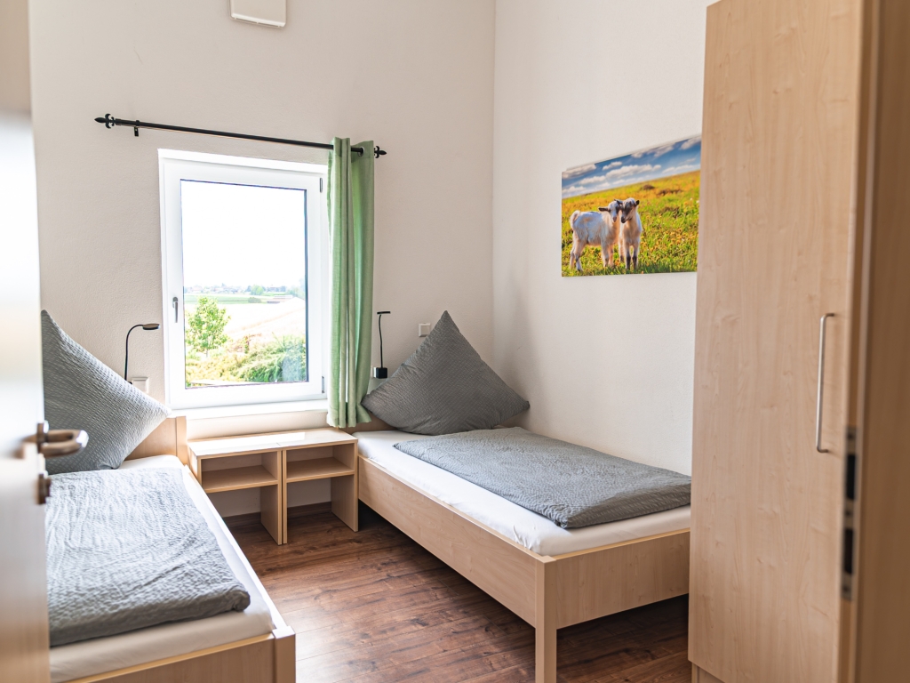 Ferienwohnung 4: Schlafzimmer mit zwei Einzelbetten, Kleiderschrank und Fenster mit grünem Vorhang