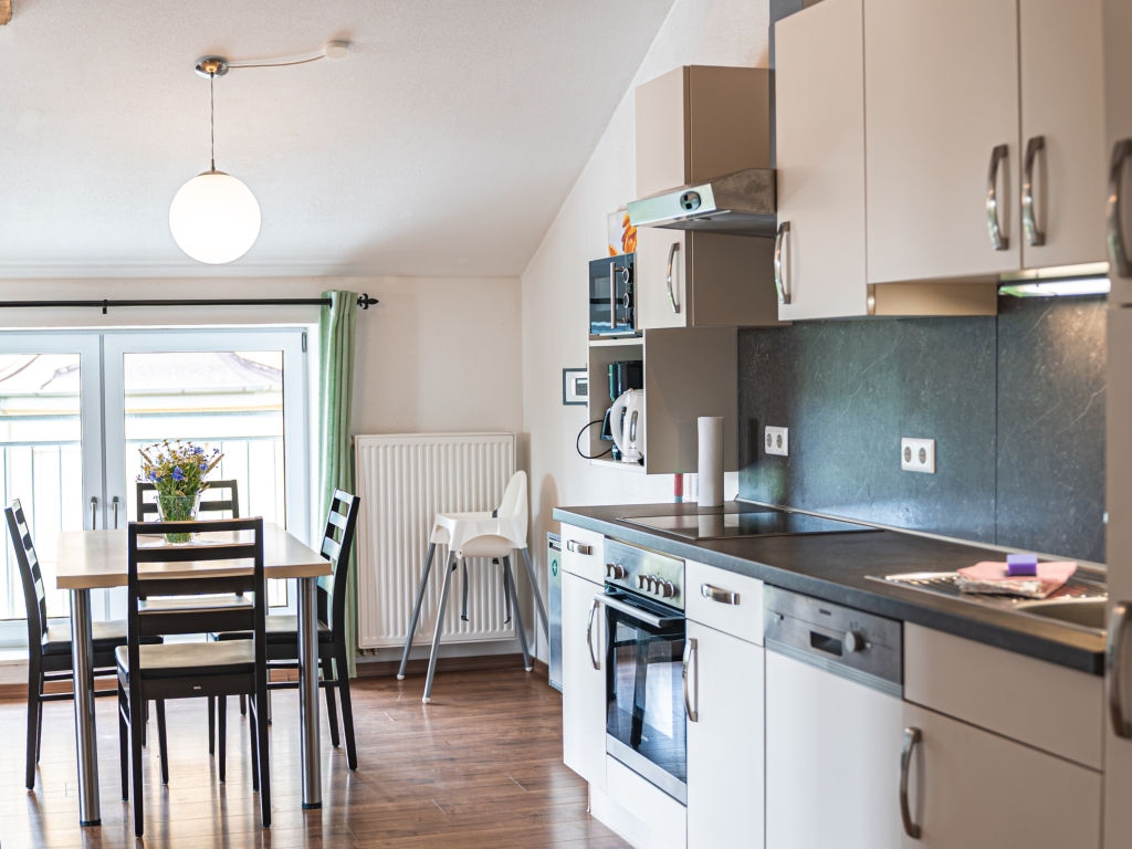 Ferienwohnung 4: Küchenzeile mit Backofen und Geschirrspüler, dahinter Esstisch mit Stühlen und Kinder-Hochstuhl