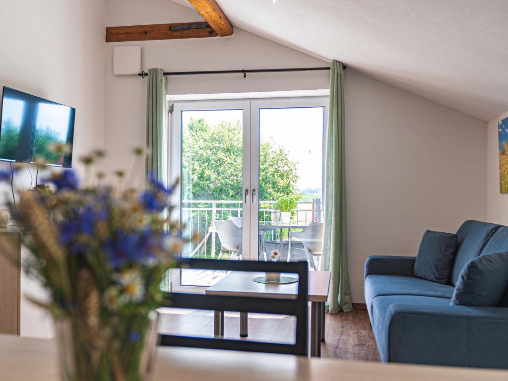 Ferienwohnung 4: Wohnbereich mit blauem Sofa, Balkontür und Fernseher unter der Dachschräge