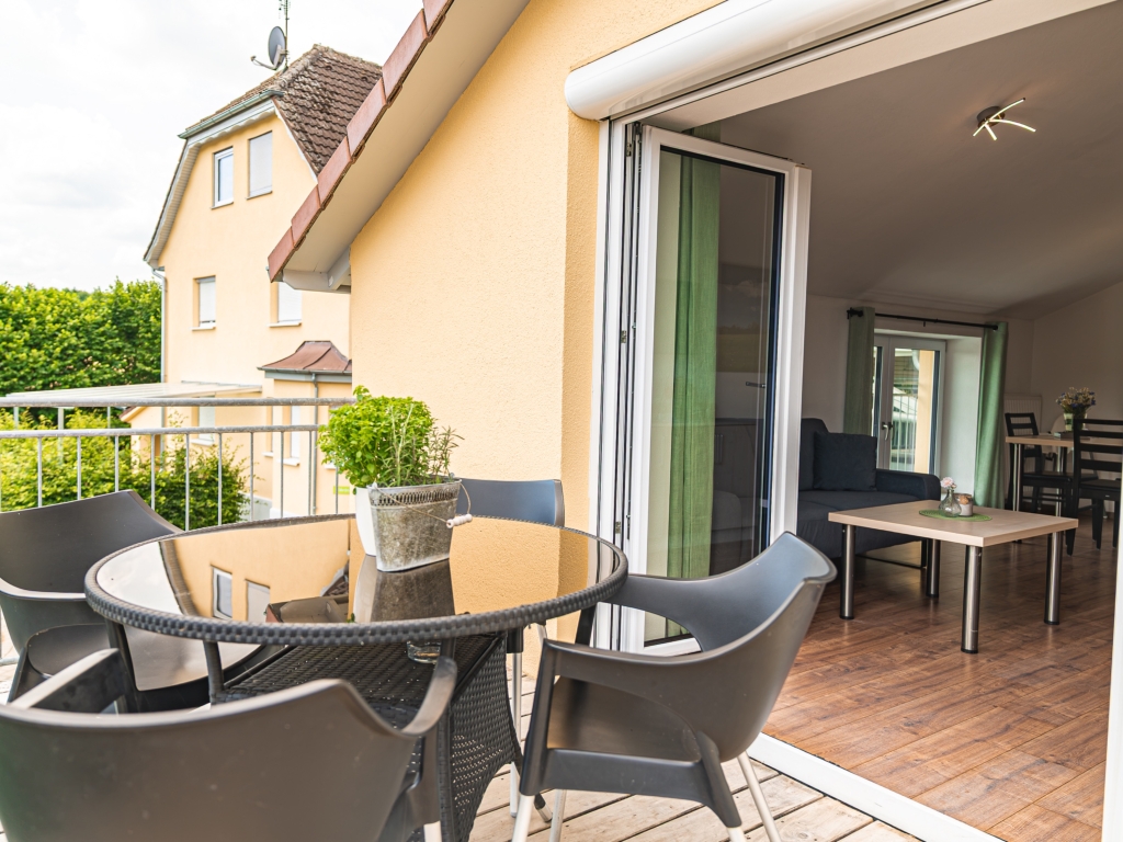 Ferienwohnung 4: Balkon mit rundem Tisch, Stühlen und Kräutertopf, daneben die offene Balkontür