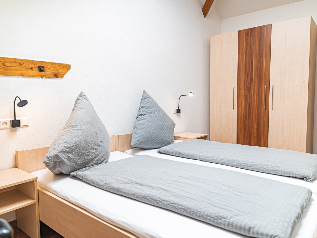Ferienwohnung 5: Schlafzimmer mit Betten in grauer Bettwäsche, Kleiderschrank und Nachttisch mit Leselampe