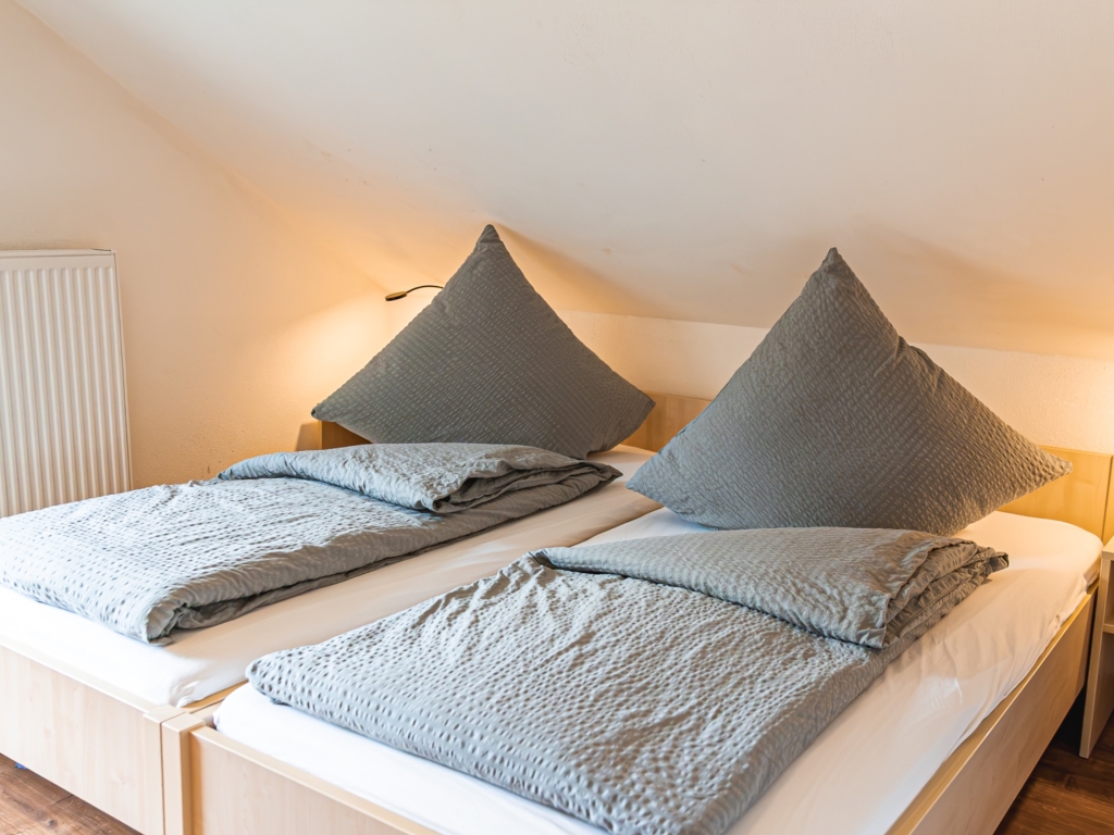 Ferienwohnung 5: Schlafzimmer unter der Dachschräge mit hellen Holzbetten und grauer Bettwäsche