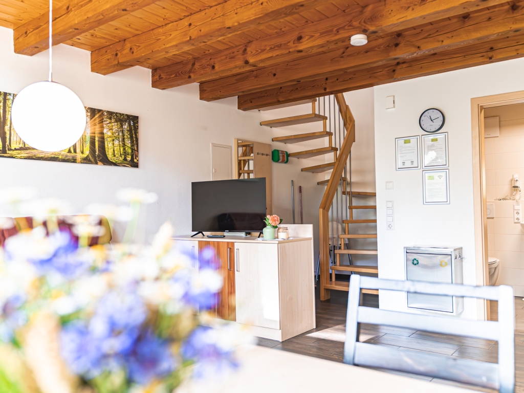 Ferienwohnung 5: Wohnbereich mit Fernseher, Holzbalkendecke und Wendeltreppe zum Obergeschoss