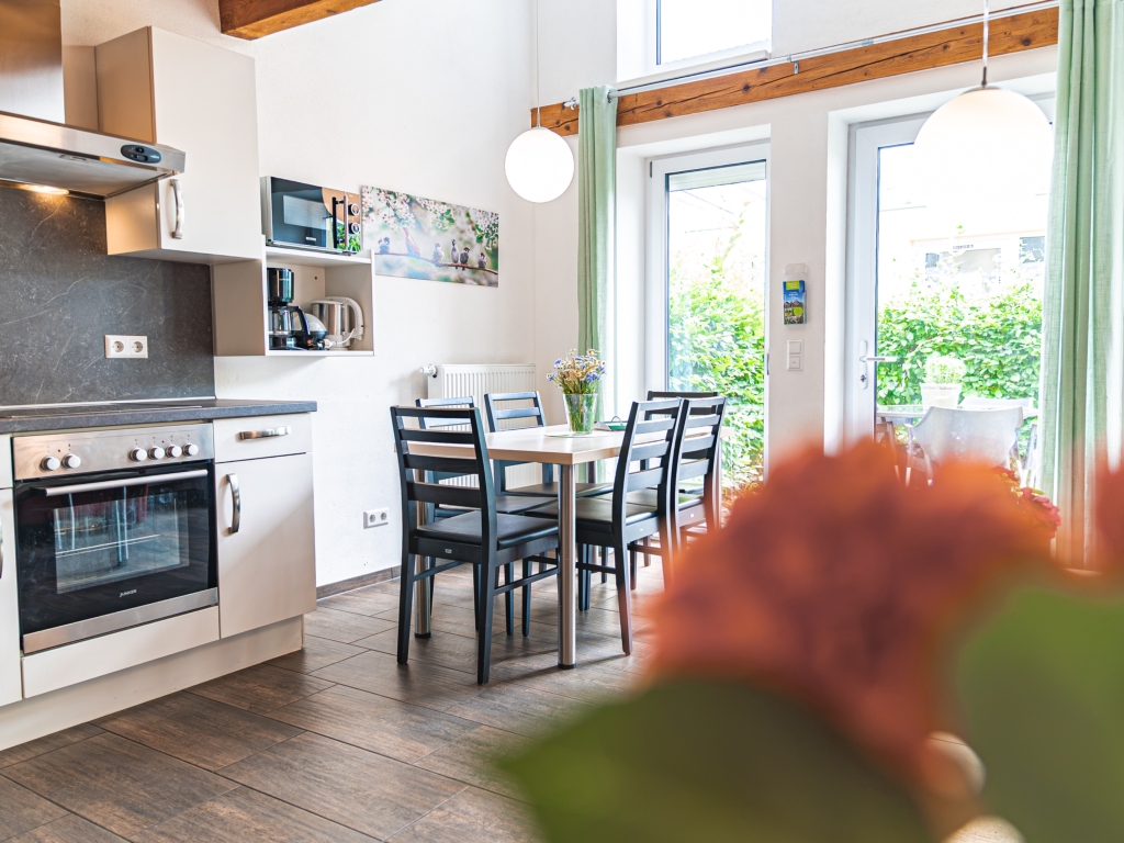 Ferienwohnung 5: Küche mit Backofen und Dunstabzugshaube, dahinter Esstisch mit Stühlen und Terrassentür