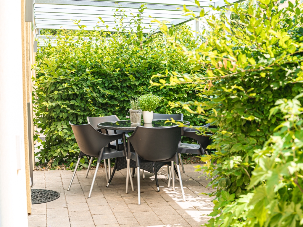 Ferienwohnung 5: Terrasse mit Tisch und Stühlen, umgeben von dichten grünen Hecken
