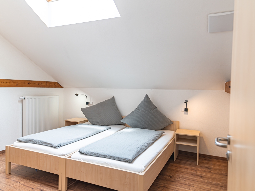 Ferienwohnung 6: Schlafzimmer unter der Dachschräge mit zwei Betten, Dachfenster und Nachttischen