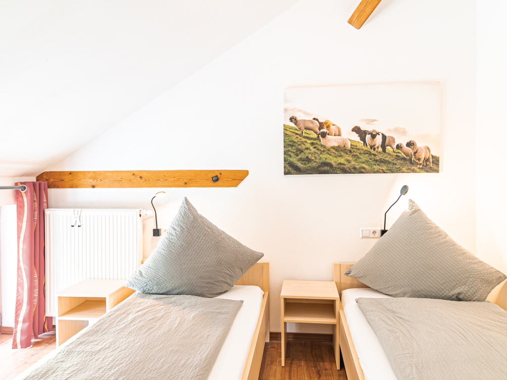 Ferienwohnung 6: Schlafzimmer mit zwei Einzelbetten, Nachttisch, Leselampen und Wandbild unter der Dachschräge